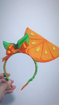 someone is holding up a paper headband with an orange flower on it and a green leaf attached to the top