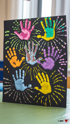 handprints are displayed on a black card with colorful paint sprinkles