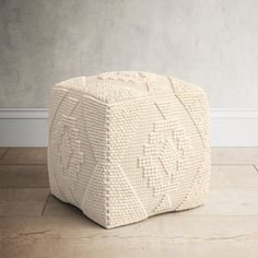 a white knitted poufce sits on the floor in front of a wall