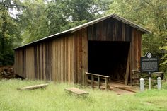 an old covered bridge in the middle of a grassy area with stairs leading up to it