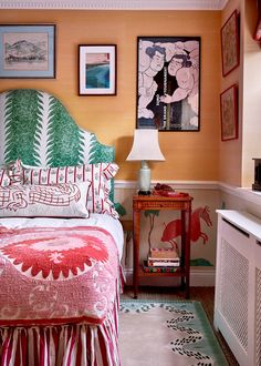 a bedroom with orange walls and pictures on the wall above the bed, along with a dresser