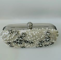 The Pearl Purse is a stylish blend of sophistication and glamour. It is crafted with precision and attention to details. This beaded purse is a must have addition to your accessory collection. It will glamorize your look and is spacious enough to carry all the essentials. The clutch comes with a detachable chain strap so you can carry it as a clutch or a shoulder & crossbody bag. Dimensions: (LxHxW): 7.5 inches x 4.7 inches x 1.97 inches Material: Pearls and Beads, Satin, Rhinestones Features: K Elegant Hand Embellished Party Bags, Elegant Beaded Rectangular Evening Bag, Glamorous Hand Embellished Evening Bag For Formal Events, Glamorous Beaded Evening Bag For Formal Occasions, Glamorous Beaded Evening Bag For Formal Events, Elegant Clutch With Pearl Handle For Reception, Elegant Bags With Pearl Handle For Reception, Elegant Pearl Handle Clutch For Reception, Silver Hand Embellished Evening Bag For Formal Occasions