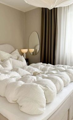 an unmade bed with white sheets and pillows in a bedroom next to a window