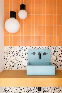 a bathroom sink sitting under two lights on top of a counter next to a tiled wall