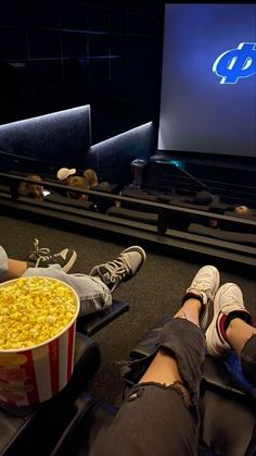 two people sitting in front of a movie screen with popcorn on the floor next to them