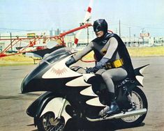 a man dressed as batman riding on the back of a black and white bat motorcycle