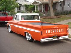 an orange and white chevy truck parked on the side of the road next to a red pickup truck