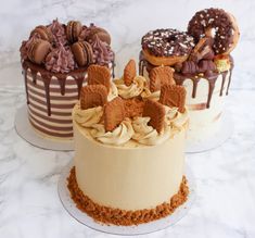 three cakes decorated with frosting and toppings on top of a marble countertop