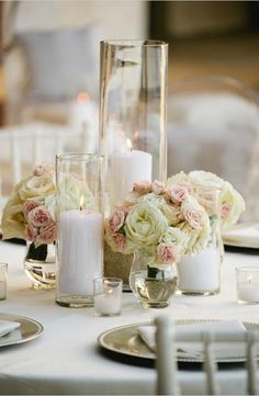 the table is set with white and pink flowers, candles, and glass vases