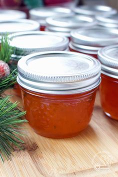 several jars filled with jam sitting on top of a wooden table next to pine branches