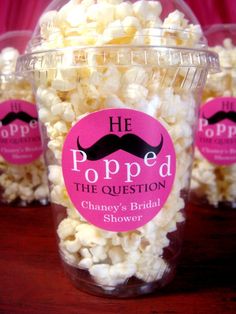 popcorn in a plastic cup with pink labels and mustaches on the label is labeled he popped the question