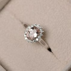 an engagement ring with a pink stone surrounded by white and clear stones on a beige background