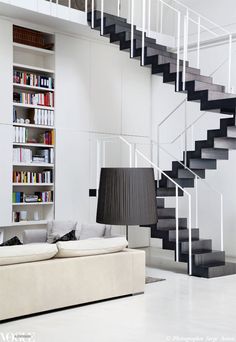 a living room filled with furniture and a book shelf next to a stair case full of books