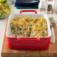 a red and white casserole dish sitting on top of a wooden cutting board