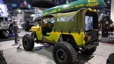 a yellow jeep is on display at an auto show with people looking around the vehicle