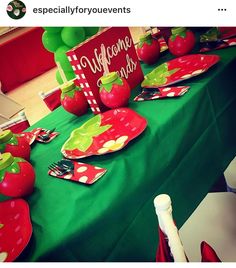 the table is set with red and green plates, napkins, and strawberries