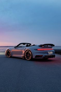 a silver sports car parked on the side of the road near the ocean at dusk