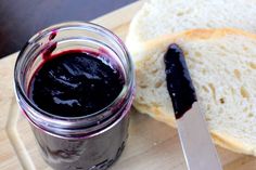 a jar of jam next to a sandwich on a wooden cutting board with a knife