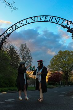 two people in graduation gowns standing under an arch