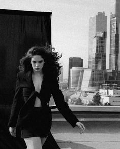 black and white photograph of woman in dress on rooftop with cityscape behind her