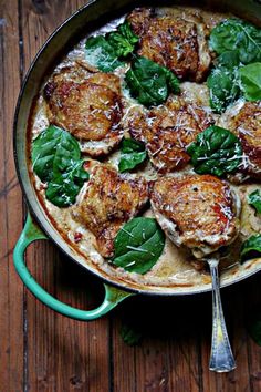 a pan filled with meat and spinach on top of a wooden table next to a fork