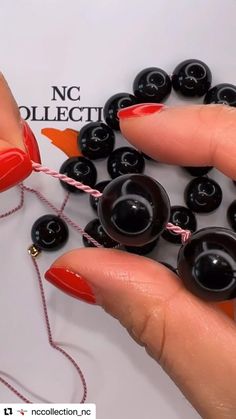 a woman's hand holding some black beads on a string and red nail polish