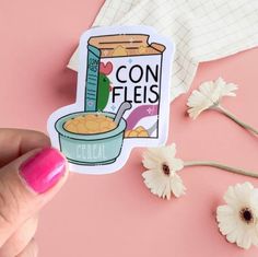 a hand holding a sticker that says con fiels cereal with flowers in the background