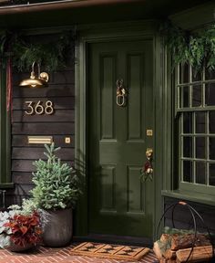 a green door with two potted plants on the front porch and an address sign