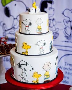 a three tiered cake decorated with cartoon characters on white frosting and red plate