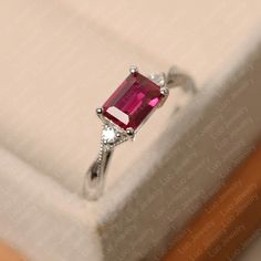 Rectangular Ruby Ring Fine Jewelry, Rectangular Ruby Ring In Fine Jewelry Style, Red Emerald Cut Birthstone Ring, Ruby Ring With Rectangular Stone For Anniversary, Emerald Cut Ruby Ring For Promise Ring, Emerald Cut Solitaire Ruby Ring In Fine Jewelry Style, Emerald Cut Red Birthstone Ring, Emerald Cut Ruby Ring With Birthstone, Anniversary White Gold Ruby Ring With Radiant Cut