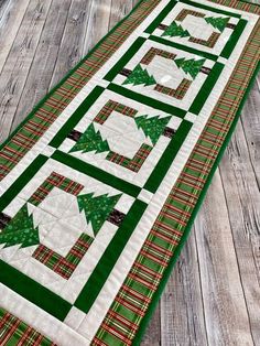 a quilted table runner with green and red plaid christmas trees on the top, sitting on a wooden floor