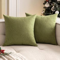 two green pillows sitting on top of a couch next to a christmas tree