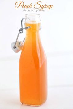 a glass bottle filled with orange juice on top of a white countertop next to a spoon