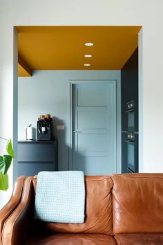 a brown leather couch sitting in front of a white wall with yellow painted ceilinging