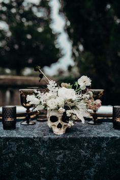 a table topped with a skull vase filled with flowers