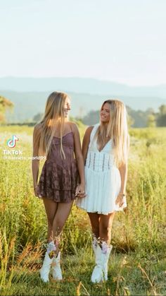 two beautiful young women standing next to each other in a grassy field with mountains in the background