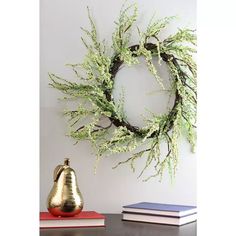 a gold vase sitting on top of a table next to a green wreath and books