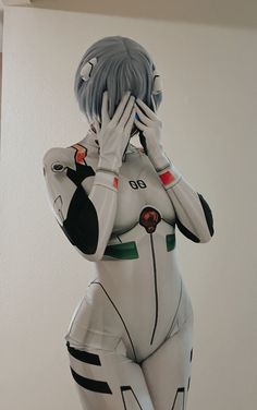 a statue of a woman covering her face with her hands and standing in front of a white wall