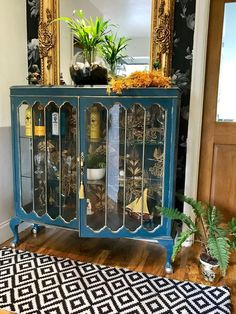 a blue cabinet with glass doors and plants on top in front of a mirror that says, hand painted by monster's dragonfly