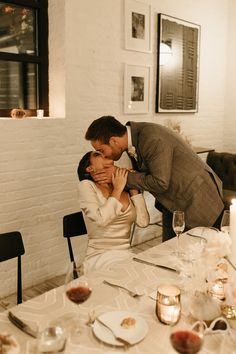 a man kissing a woman at a table with candles and plates on the dining room table