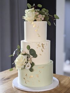 a three tiered wedding cake with white flowers on the top and green leaves on the bottom