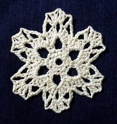 a crocheted snowflake is shown on a dark blue surface with white yarn