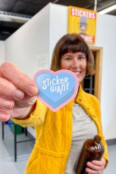 a woman holding up a sticker with the word sticker giant on it in front of her