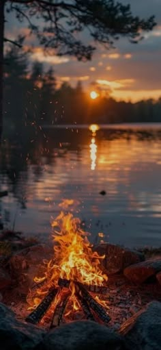 a campfire is lit up by the water at sunset or dawn with its reflection in the water