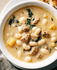 a bowl of soup with meatballs and spinach in it next to a piece of bread