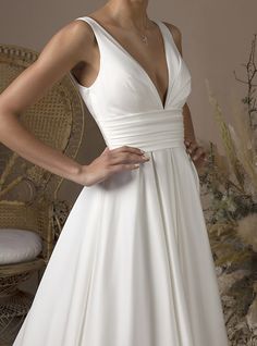 a woman in a white wedding dress standing next to a wicker chair and flower arrangement