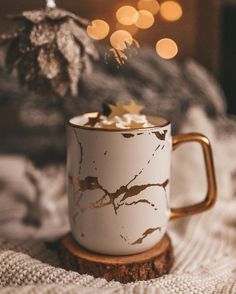 a white and gold coffee mug on top of a wooden table next to a christmas tree