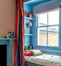 a bedroom with blue walls and colorful curtains on the window sill, along with a bed in front of a fireplace