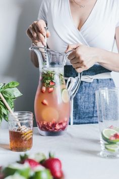 a woman pours water into a pitcher with strawberries and mint leaves in it