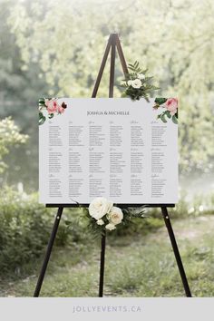 a sign with flowers and greenery on it for an outdoor wedding ceremony in the woods